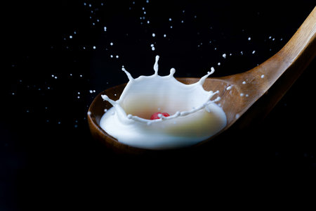 fresh raspberry splashing milk on a wooden spoon, splash effect with black backgroundの写真素材