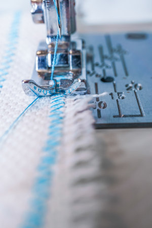 close-up of sewing machine needle with blue thread sewing on a white fabricの写真素材
