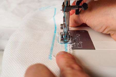close-up of woman's hands sewing a fabric with blue thread on a sewing machineの写真素材