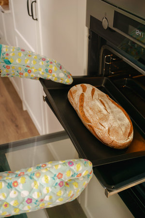 loaf of bread in the oven tray with oven mitts