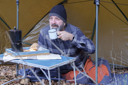 man with beard and hat drinking coffee in his winter tentの写真素材