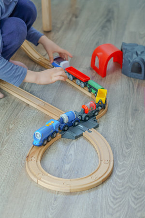 unrecognizable child playing with a wooden train on the floor in his bedroom