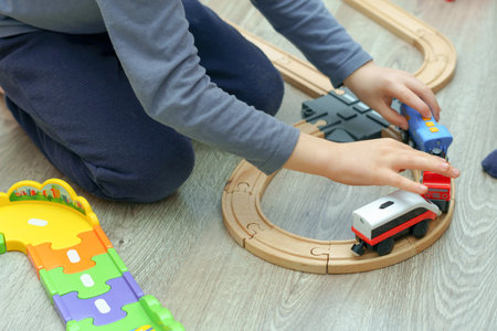 unrecognizable child playing with a wooden train on the floor in his bedroom