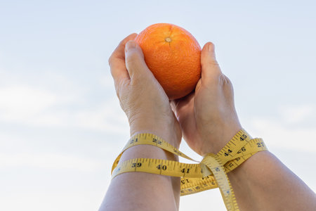 woman holding an orange with her arms tied with a tape measure, diet slave conceptの写真素材