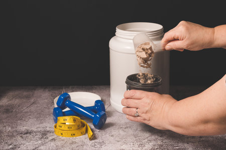 woman pouring a scoop of protein powder into an insulated shaker on a black background