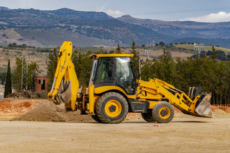 yellow excavator working with mountains in the backgroundの写真素材