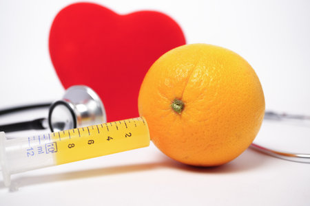orange with a syringe full of juice, a stethoscope and a red heart, heart health concept white backgroundの写真素材