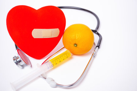 orange with a syringe full of juice, a stethoscope and a red heart, heart health concept white backgroundの写真素材