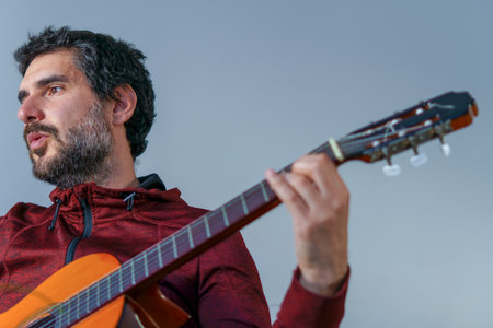 young bearded man playing spanish guitar cc blue background with copy spaceの写真素材