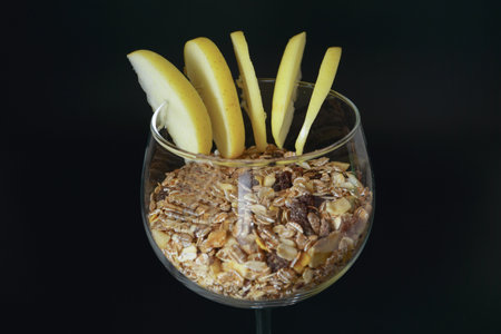 glass cup with muesli, apple and milk isolated on black background