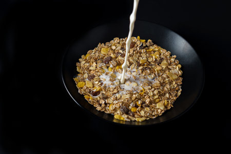 milk dripping on a plate of muesli isolated on a black background and copy spaceの写真素材