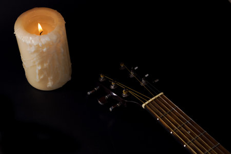 Spanish guitar neck with a candle in the background on a black backgroundの写真素材
