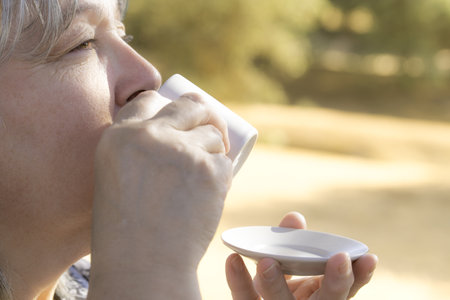 woman seen in profile drinking a cup of coffee in a field with her face illuminated by the sunの写真素材