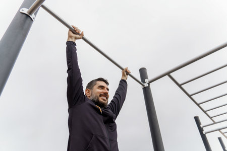young man dressed in black training on a pull-up bar in an outdoor gymの写真素材