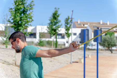 profile view of a bearded man with sunglasses stretching his back with an elastic strapの写真素材