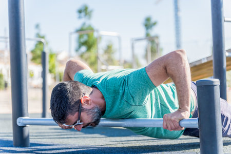 man seen in profile with beard and sunglasses doing push-ups on a bar on the floorの写真素材