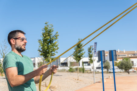 Bearded man with sunglasses seen in profile training his arms with an elastic fitness band in an outdoor gym.の写真素材