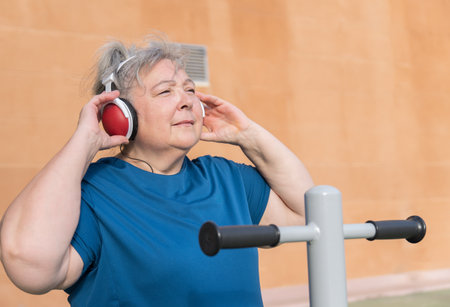 active obese elderly woman in sportswear working out on a park machine while listening to music on her headphonesの写真素材