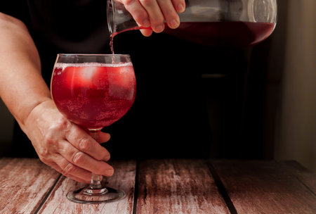 waitress dressed in black serving a glass of sparkling red summer wine on the rocks from a glass decanterの写真素材