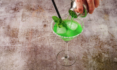 hand of a woman serving a mint cocktail with ice straw and mint leaves with a cocktail shakerの写真素材