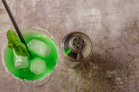 top view of a green cocktail with mint ice and straw the edges of the glass have icing sugar and a cocktail shaker to accompany itの写真素材