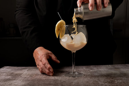 waitress dressed in black serving a banana cocktail with ice and a slice of banana with a cocktail shakerの写真素材