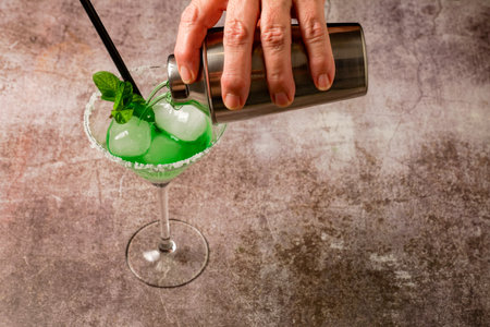 hand of a woman serving a mint cocktail with ice straw and mint leaves with a cocktail shakerの写真素材