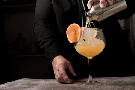 waitress dressed in black serving an orange cocktail with ice and orange slice with a cocktail shakerの写真素材