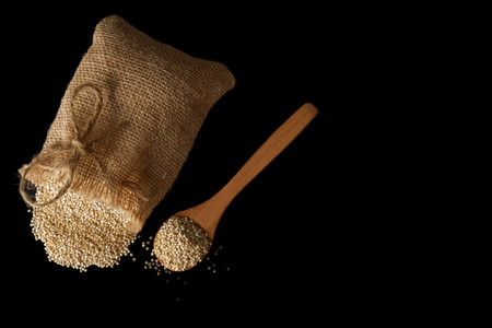 wooden spoon with the protein-rich superfood quinoa (Chenopodium quinoa) and a cloth bag with raw seeds isolated on black background and copy spaceの写真素材