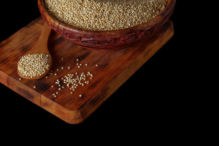 wooden spoon with quinoa and wooden bowl full of seeds isolated on black background and copy spaceの写真素材