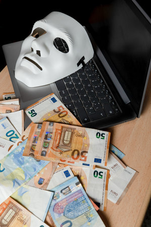 on a laptop there is a white mask and a pile of euro banknotes, cybercrime concept.の写真素材