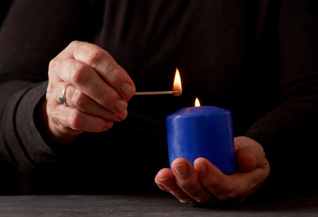 hands of a woman lighting a blue candle with a match with a black background and copy spaceの写真素材