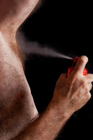 man with chest hair spraying deodorant in his armpit with a black background for copy spaceの写真素材