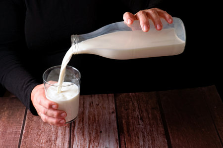 hands of a woman pouring fresh milk into a glass, with a glass bottle , black background and copy spaceの写真素材