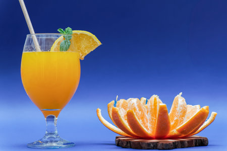 natural orange juice with orange slice, straw and mint .with orange cut into segments on a wooden disk with blue background and copy spaceの写真素材