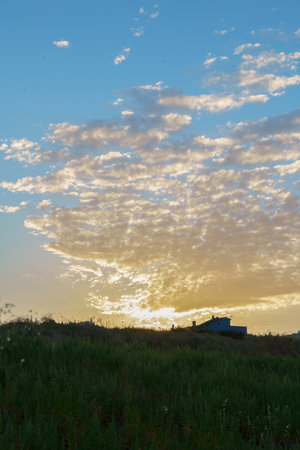 colorful sunrise with clouds with a meadow and a house in the background, lights and shadowsの写真素材