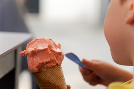 unrecognizable child eating strawberry ice cream with a spoonの写真素材