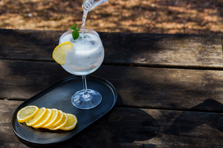 top view of a bottle of tonic poured over a glass with ice, slice of lemon and mint leaves, preparation of a gin and tonic.の写真素材