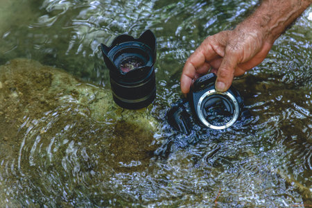 a man cleans the sensor of his reflex camera in the water of a river by flooding it from the insideの写真素材