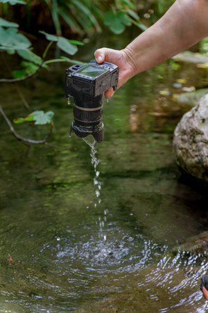 a reflex camera accidentally falls into the river, a man pulls it out of the water dripping wet.の写真素材