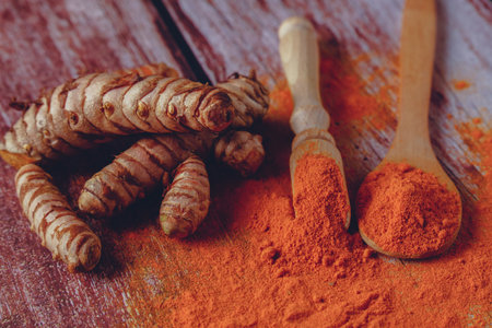 fresh turmeric root and ground turmeric in a wooden spoon poured out on a wooden tableの写真素材