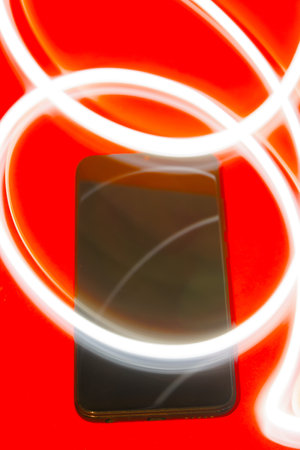 mobile phone on a red background with white light strokes making circles on it.