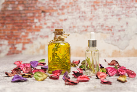 bottle and dropper with rosemary oil with fresh branches inside surrounded by colorful flower leaves and a brick wall in the backgroundの写真素材