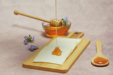 drizzle of honey dripping on cheese slices with fresh rosemary branches in bloom and a glass bowl with rosemary honey.の写真素材