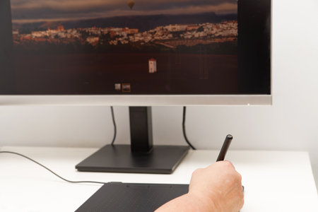 Woman hand working on her computer with a digital graphic tablet, in the background a monitor with an imageの写真素材