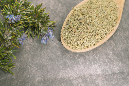 ground rosemary in a wooden spoon together with a branch of fresh rosemary in bloomの写真素材