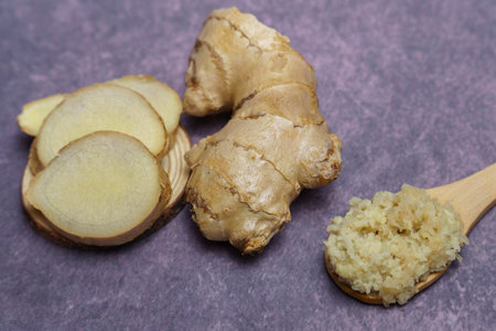 ground ginger in a wooden spoon with fresh ginger root cut into slicesの写真素材
