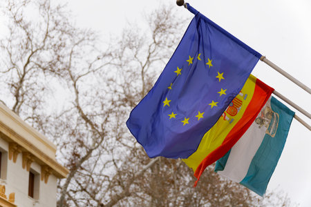 flags of spain, europe and andalucia waving in the wind in a public building