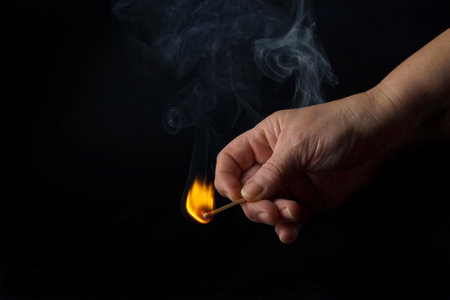 close-up of a woman's hand lighting a match isolated on black backgroundの写真素材