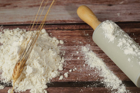pile of flour with an ear of wheat on top of it, next to a rolling pin, on a wooden table and copy spaceの写真素材